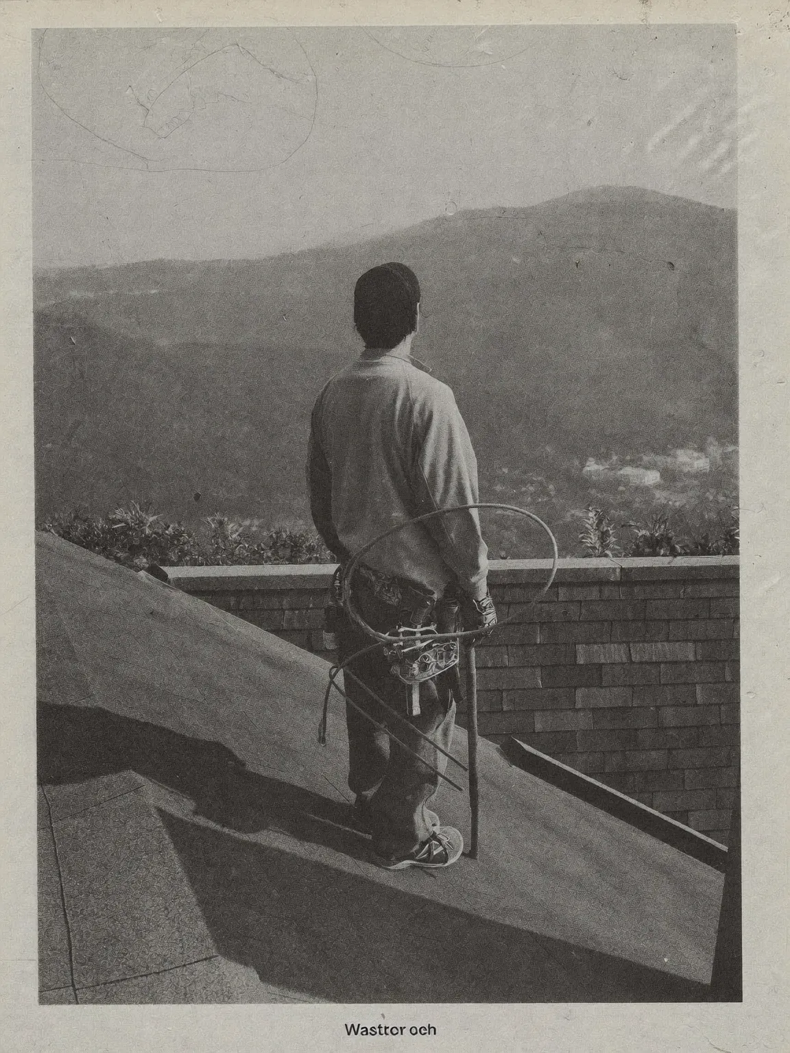 Black and white photograph of a roofing contractor on a residential roof, mountains in the distance