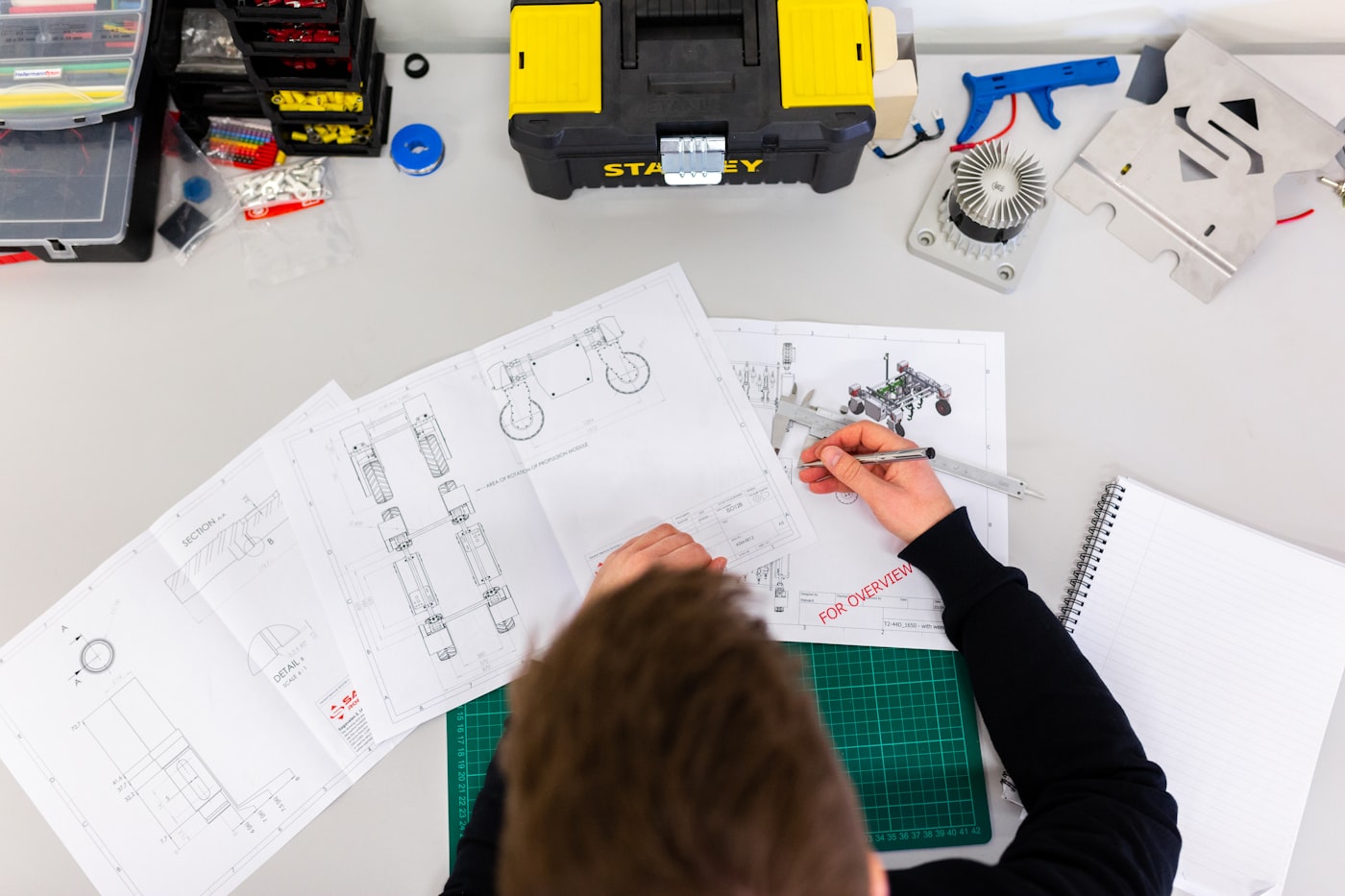Overhead view of hands working over technical drawings and tools