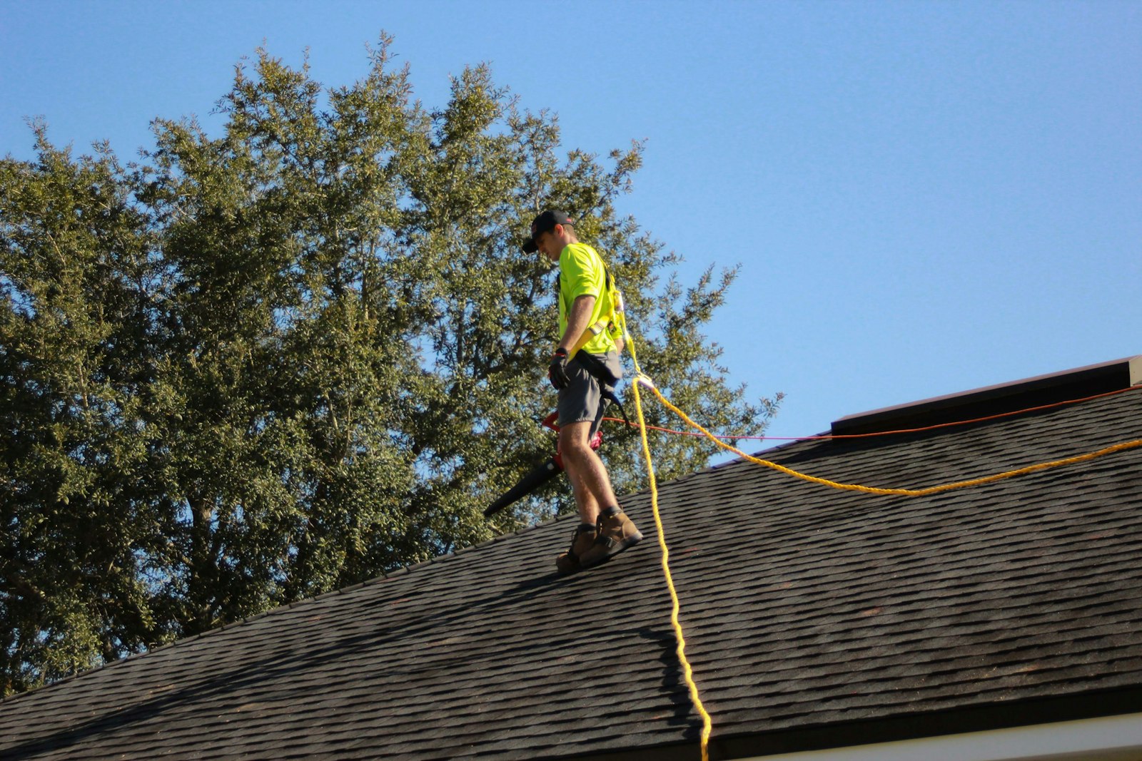 A roofer with a safety line working across a shingle roof