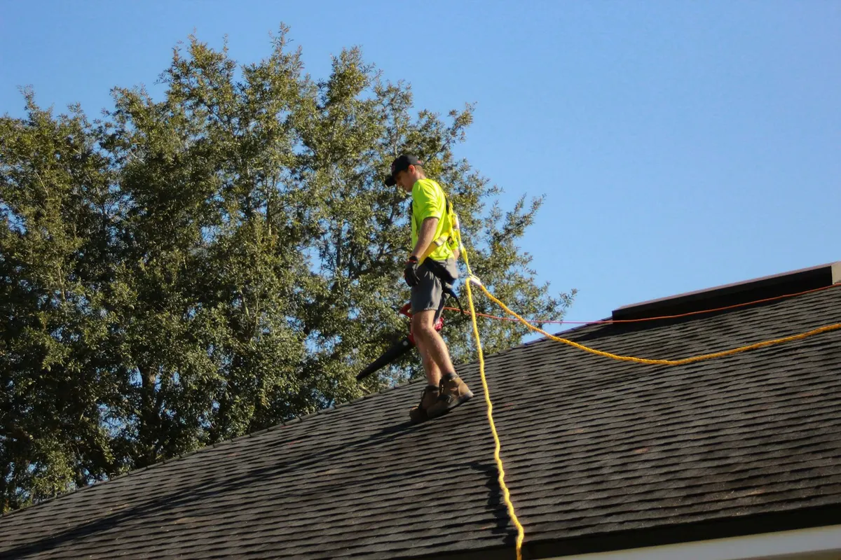 A roofer with a safety line working across a shingle roof