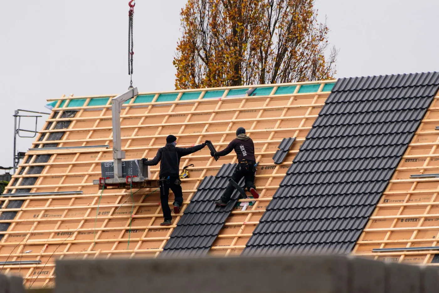A crew installing dark roof tiles course by course